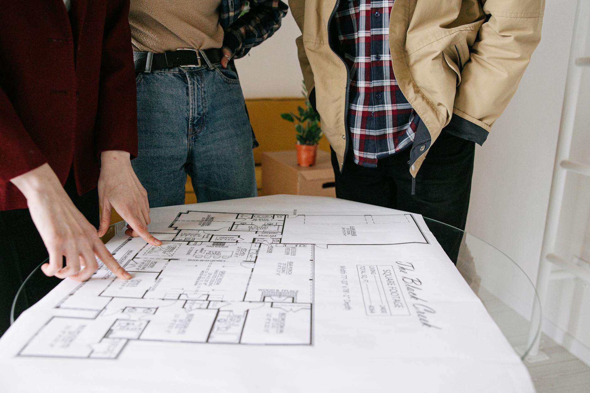 three people standing near blueprint on glass table